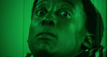 Movie still from “Watermelon Man” (1970), directed by Melvin Van Peebles – A man's face in green light; Extreme Close Up shot, Low angle