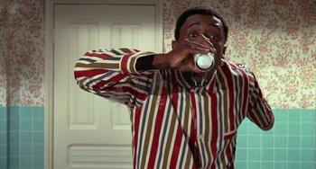 Movie still from “Watermelon Man” (1970), directed by Melvin Van Peebles – A man in a striped shirt drinking a cup of coffee; Medium shot, High angle