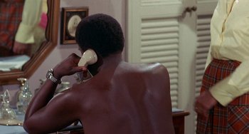 Movie still from “Watermelon Man” (1970), directed by Melvin Van Peebles – A man talking on a phone while sitting at a table; Medium shot, High angle