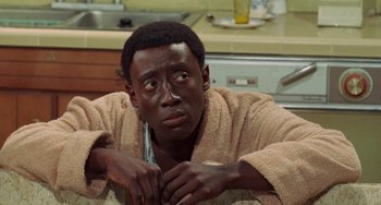 Movie still from “Watermelon Man” (1970), directed by Melvin Van Peebles – A man in a robe is sitting in a kitchen; Close Up shot, High angle