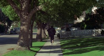 Movie still from “Watermelon Man” (1970), directed by Melvin Van Peebles – A person walking down a sidewalk next to trees; Wide shot, High angle