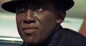 Movie still from “Watermelon Man” (1970), directed by Melvin Van Peebles – A person wearing a suit and a hat; Close Up shot, Low angle
