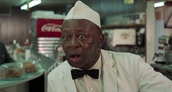 Movie still from “Watermelon Man” (1970), directed by Melvin Van Peebles – An older man wearing a white hat and a white jacket; Close Up shot, Low angle