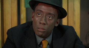 Movie still from “Watermelon Man” (1970), directed by Melvin Van Peebles – A person wearing a suit and a hat; Close Up shot, Low angle