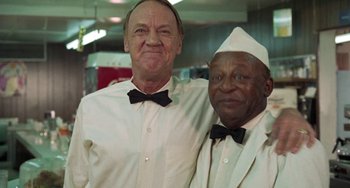 Movie still from “Watermelon Man” (1970), directed by Melvin Van Peebles – A couple of men standing next to each other; Medium shot, Low angle