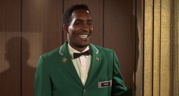 Movie still from “Watermelon Man” (1970), directed by Melvin Van Peebles – A man wearing a green jacket and a bow tie; Medium shot, Low angle