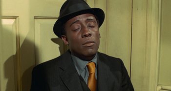 Movie still from “Watermelon Man” (1970), directed by Melvin Van Peebles – A man in a suit and tie with his eyes closed; Close Up shot, High angle
