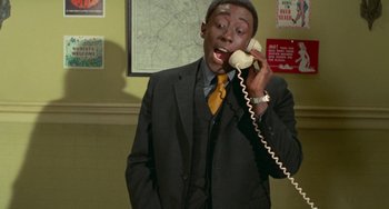 Movie still from “Watermelon Man” (1970), directed by Melvin Van Peebles – A man talking on a phone while wearing a suit and tie; Medium shot, Low angle