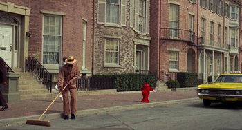 Movie still from “Watermelon Man” (1970), directed by Melvin Van Peebles – An old man in a suit and hat is standing on the sidewalk by a red fire hydrant; Wide shot, High angle