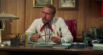 Movie still from “Watermelon Man” (1970), directed by Melvin Van Peebles – A man sitting at a desk wearing a white lab coat; Medium shot, Low angle