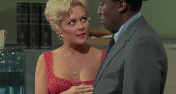 Movie still from “Watermelon Man” (1970), directed by Melvin Van Peebles – A woman in a red dress and a man in a gray suit; Close Up shot, Over the shoulder angle