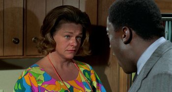 Movie still from “Watermelon Man” (1970), directed by Melvin Van Peebles – An older woman wearing a colorful shirt is looking at a younger man; Close Up shot, Over the shoulder angle