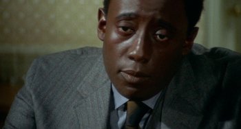 Movie still from “Watermelon Man” (1970), directed by Melvin Van Peebles – A person wearing a suit and tie; Close Up shot, High angle