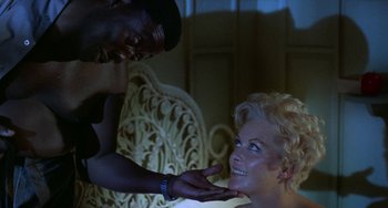 Movie still from “Watermelon Man” (1970), directed by Melvin Van Peebles – A man touching the face of a woman in front of a chair; Close Up shot, Low angle