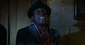 Movie still from “Watermelon Man” (1970), directed by Melvin Van Peebles – A man in a suit and a hat is smiling; Close Up shot, Low angle