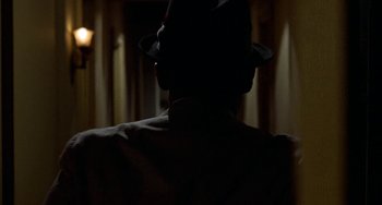Movie still from “Watermelon Man” (1970), directed by Melvin Van Peebles – A man wearing a hat is standing in the dark; Close Up shot, Over the shoulder angle