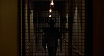 Movie still from “Watermelon Man” (1970), directed by Melvin Van Peebles – A person walking down a hallway with a light hanging from the ceiling; Wide shot, Low angle