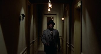 Movie still from “Watermelon Man” (1970), directed by Melvin Van Peebles – A man in a suit and hat walking down a hall way; Wide shot, Low angle