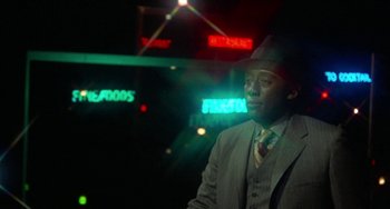 Movie still from “Watermelon Man” (1970), directed by Melvin Van Peebles – A man in a suit and hat standing in front of neon signs; Close Up shot, Over the shoulder angle