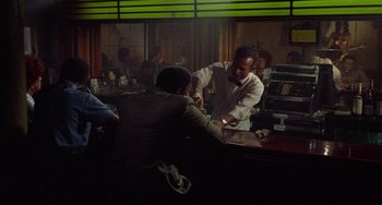 Movie still from “Watermelon Man” (1970), directed by Melvin Van Peebles – A man standing at a bar talking to another man; Wide shot, Over the shoulder angle