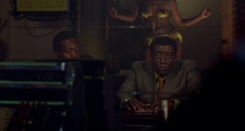 Movie still from “Watermelon Man” (1970), directed by Melvin Van Peebles – A man sitting at a table with a drink in his hand; Medium shot, Over the shoulder angle