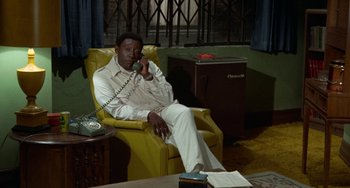 Movie still from “Watermelon Man” (1970), directed by Melvin Van Peebles – A man sitting in a chair talking on the phone; Medium shot, High angle