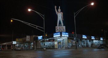 Movie still from “Wayne's World” (1992), directed by Penelope Spheeris – A large statue of a man is on top of a building; Extreme Wide shot, Low angle
