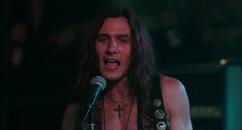 Movie still from “Wayne's World” (1992), directed by Penelope Spheeris – A man with long black hair is singing into a microphone; Close Up shot, Low angle