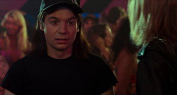 Movie still from “Wayne's World” (1992), directed by Penelope Spheeris – A man in a black shirt wearing a black hat; Close Up shot, Over the shoulder angle