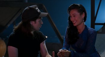 Movie still from “Wayne's World” (1992), directed by Penelope Spheeris – A man and a woman sitting next to each other holding hands; Medium shot, Over the shoulder angle