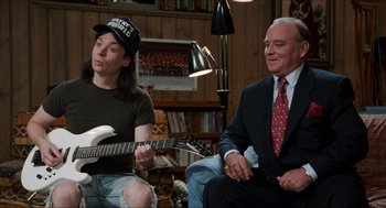 Movie still from “Wayne's World” (1992), directed by Penelope Spheeris – A man sitting next to another man holding a guitar; Medium shot, Over the shoulder angle