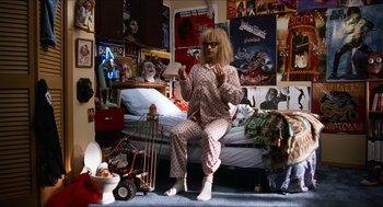 Movie still from “Wayne's World” (1992), directed by Penelope Spheeris – A man sitting on a bed in a room with a lot of posters on the wall; Wide shot, Overhead angle