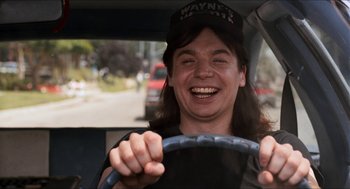 Movie still from “Wayne's World” (1992), directed by Penelope Spheeris – A woman smiles while sitting in the drivers seat of a car; Medium shot, High angle
