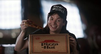 Movie still from “Wayne's World” (1992), directed by Penelope Spheeris – A man holding a box of pizza in front of his face; Medium shot, Low angle