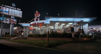 Movie still from “Wayne's World” (1992), directed by Penelope Spheeris – A night time view of a restaurant with a hockey player on top of the building; Extreme Wide shot, High angle