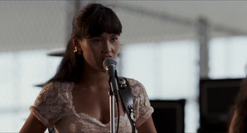 Movie still from “Wayne's World” (1992), directed by Penelope Spheeris – A woman is holding a microphone in front of her face; Close Up shot, Over the shoulder angle