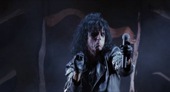 Movie still from “Wayne's World” (1992), directed by Penelope Spheeris – A man in a black leather jacket holding a microphone; Medium shot, Low angle