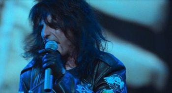 Movie still from “Wayne's World” (1992), directed by Penelope Spheeris – A person with long hair is holding a microphone; Close Up shot, Low angle