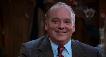 Movie still from “Wayne's World” (1992), directed by Penelope Spheeris – An older man wearing a suit and tie smiling; Close Up shot, High angle