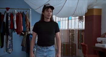 Movie still from “Wayne's World” (1992), directed by Penelope Spheeris – A man with long black hair wearing a black hat; Medium shot, Over the shoulder angle
