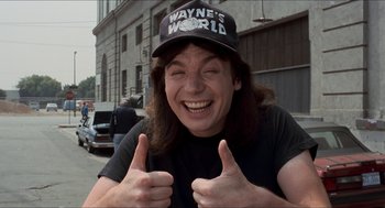 Movie still from “Wayne's World” (1992), directed by Penelope Spheeris – A man giving two thumbs up in front of a building; Medium shot, Low angle