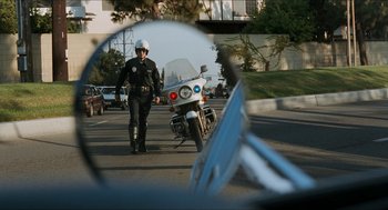 Movie still from “Wayne's World” (1992), directed by Penelope Spheeris – A police officer on the side of the road with a motorcycle behind him; Wide shot, Low angle