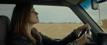 Movie still from “We Summon the Darkness” (2019), directed by Marc Meyers – A woman sitting in the drivers seat of a car driving down a dirt road; Close Up shot, Over the shoulder angle