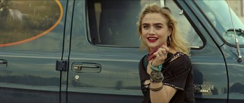 Movie still from “We Summon the Darkness” (2019), directed by Marc Meyers – A woman in a black shirt holding a candy bar; Close Up shot, Over the shoulder angle