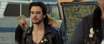 Movie still from “We Summon the Darkness” (2019), directed by Marc Meyers – A man with long black hair and a black leather jacket; Close Up shot, Over the shoulder angle