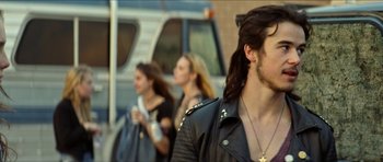 Movie still from “We Summon the Darkness” (2019), directed by Marc Meyers – A man with long black hair wearing a leather jacket; Close Up shot, Over the shoulder angle