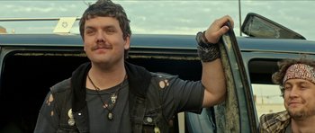 Movie still from “We Summon the Darkness” (2019), directed by Marc Meyers – A man in a black shirt is leaning against a car; Close Up shot, Over the shoulder angle