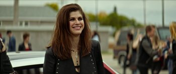 Movie still from “We Summon the Darkness” (2019), directed by Marc Meyers – A woman with long brown hair smiles for the camera; Close Up shot, Over the shoulder angle