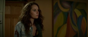 Movie still from “We Summon the Darkness” (2019), directed by Marc Meyers – A woman with long brown curly hair looking to her left; Close Up shot, Over the shoulder angle