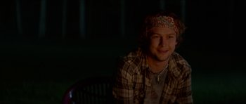 Movie still from “We Summon the Darkness” (2019), directed by Marc Meyers – A man with a bandana on his head is smiling for the camera; Medium shot, Over the shoulder angle